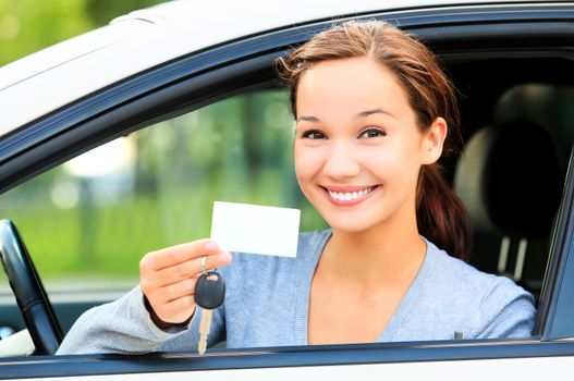 Happy girl in a car showing a key and an empty white card for your message.
