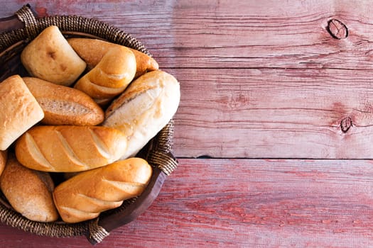 Bread basket filled with freshly baked golden crusty rolls in assorted shapes viewed overhead on rustic wooden boards with copyspace