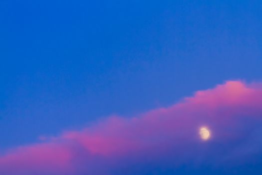 Moon under pink cloud on blue sky background