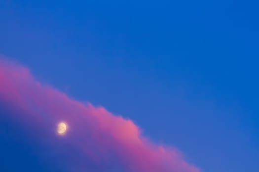 Moon under pink cloud on blue sky background