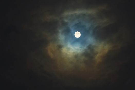 Full moon shines through dramatic sky surrounded clouds