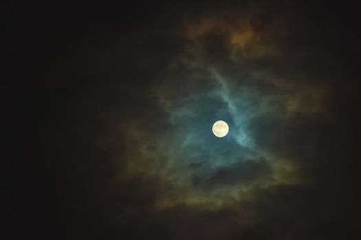 Full moon shines through dramatic sky surrounded clouds
