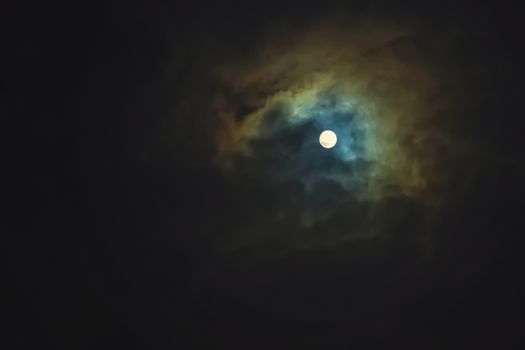 Full moon shines through dramatic sky surrounded clouds