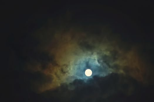Full moon shines through dramatic sky surrounded clouds