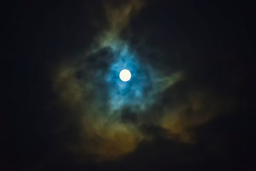 Full moon shines through dramatic sky surrounded clouds