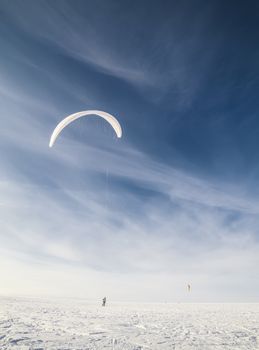 Kite boarder in snowy countryside field with cloudscape background, winter scene