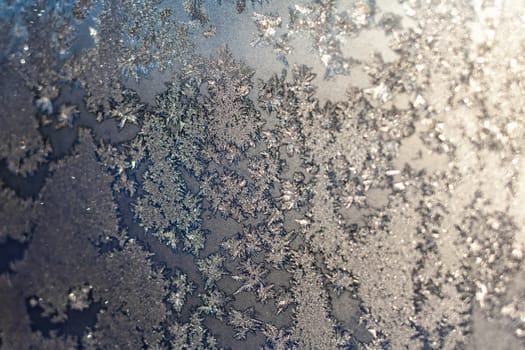 Frozen snowflakes and frost magic pattern with sunlight on Christmas winter window. Colored in gray or silver and blue tone. Selective focus with blur edges of image
