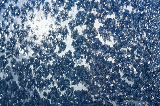 Ice snowflakes and frost pattern over the sun on frozen Christmas winter window. Colored in blue tone. Selective focus at center with blur edges of image