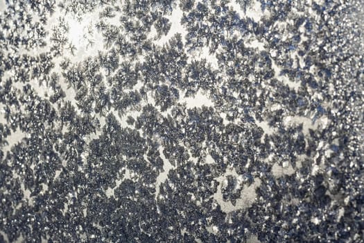 Ice snowflakes and frost pattern over the sun on frozen Christmas winter window. Colored in gray or silver tone. Selective focus at center with blur edges of image