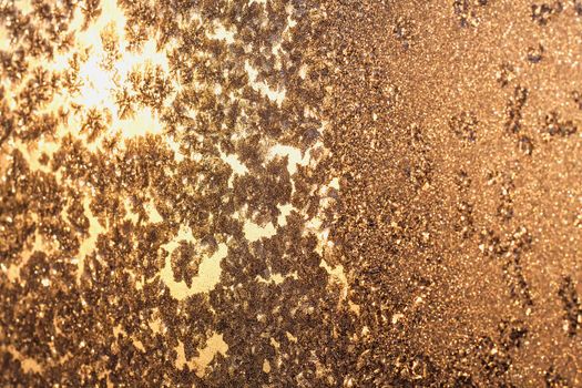 Frozen snowflakes and frost over the sun on frozen Christmas winter window. Colored in brown tone. Selective focus at center with blur edges of image