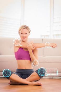 Happy blonde sitting in lotus pose stretching arms  against fitness interface