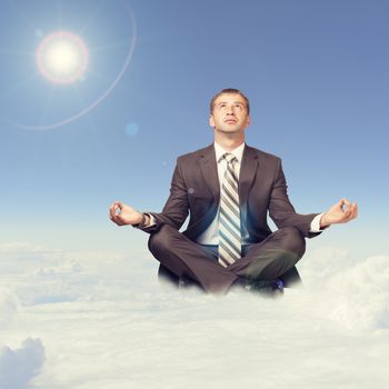 Businessman sitting in lotus position on cloud and looking up