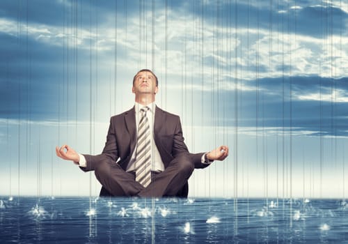 Businessman sitting in lotus position on water in sea and looking up