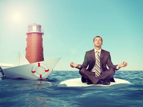 Businessman sitting in lotus position with paper boat and lighthouse in sea and looking at camera