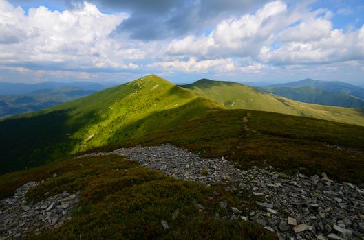 Mountain range with green grassy hills and light patches and rocks on the foreground