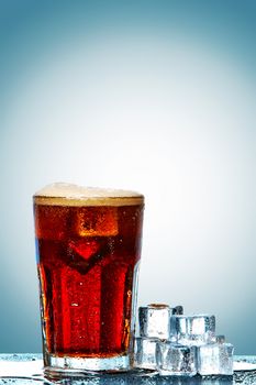 Glass of cola with ice cubes on a blue background