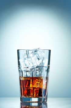 Glass of cola with ice cubes on a blue background