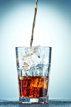 Cola pouring in a glass  with ice on a blue background