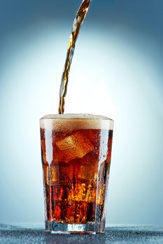 Cola pouring in a glass  with ice on a blue background