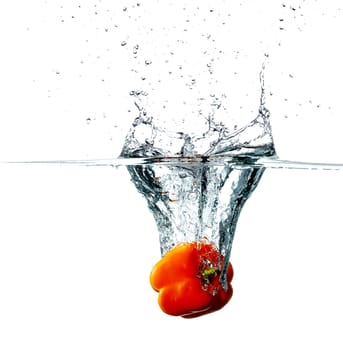 Fresh red pepper drops into a water, isolated on white background