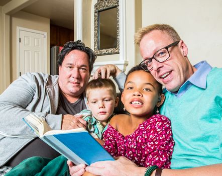 An attractive gay couple reads to their children in living room
