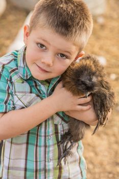 Smiling boy outside hugs his pet chicken