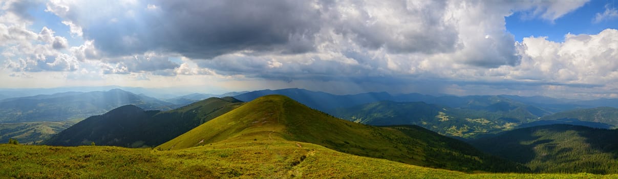 Panoramic mountains landscape with grassy range and cloudy sky and sun rays