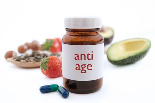 Medecine jar with anti aging pills surrounded by nutritious superfoods including avocado, pumpkin seeds and berries