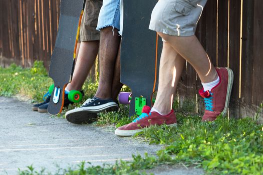 Longboarders feet standing along an urban fence line with their skateboards. Shallow depth of field.