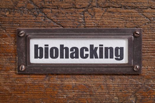 biohacking -  managing one's own biology using a combination of medical, nutritional and electronic techniques - file cabinet label, bronze holder against grunge and scratched wood