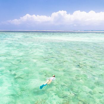 Young woman snorkeling in clear shallow sea of tropical lagoon with turquoise blue water and coral reef,  near exotic island. Mnemba island, Zanzibar, Tanzania.