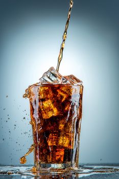 Cola pouring in a glass  with ice on a blue background