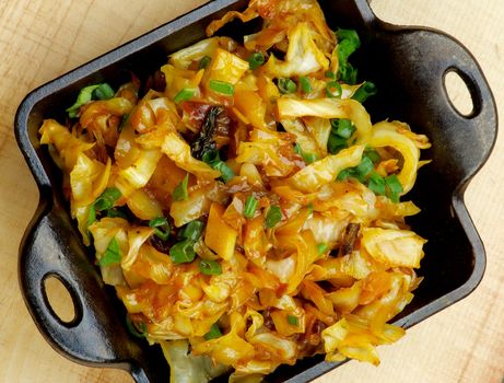 Homemade Fried Cabbage with Spring Onion in Black Frying Pan on Wooden background. Top View