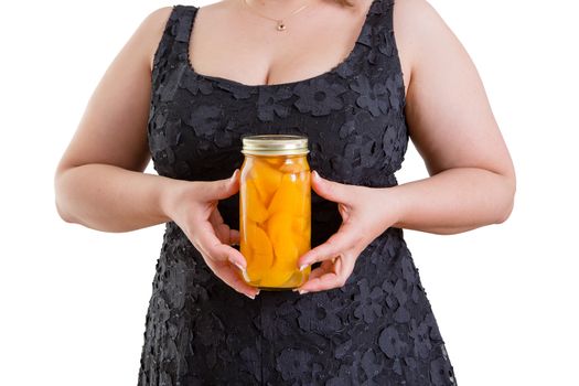 Overweight woman in a black dress holding a mason jar full of delicious orange homemade peaches in a diet and nutrition concept, close up torso view on white