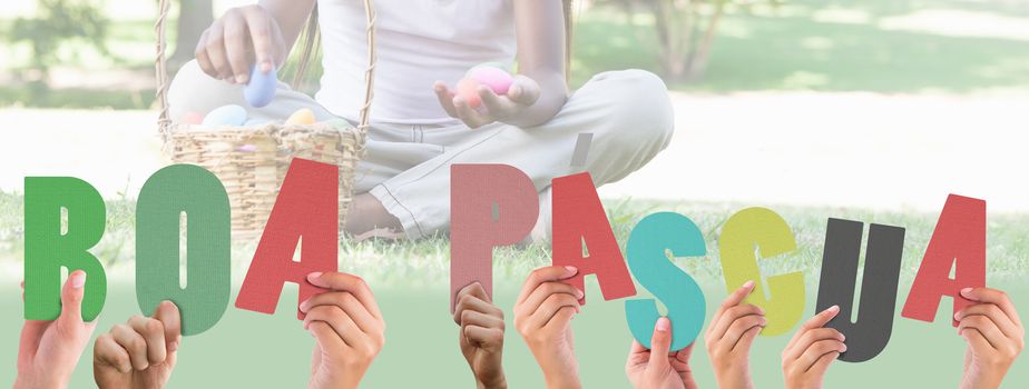 Hands holding up boa pasqua against little girl sitting on grass counting easter eggs smiling at camera