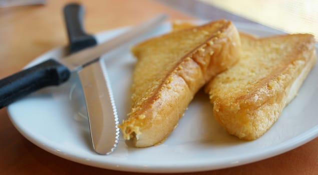 Baked bread with butter and  two knives placed on plate.                               