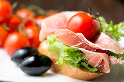 thin slices of prosciutto with mixed olives and tomato on bread