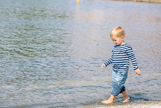 Little preschool boy walking on shore outdoors