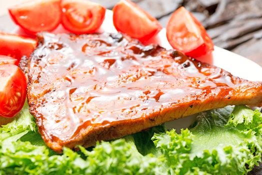 Delicious barbecued ribs seasoned with a spicy basting sauce and served with tomatoes on salad leafs in a country kitchen