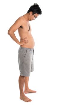 Full length Asian man looking at his fat belly, standing isolated on white background.