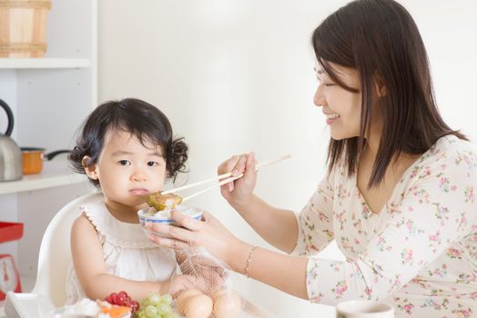 Asian mother feeding her child at home.