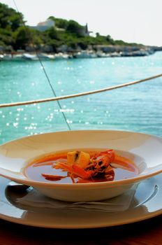 Stewed Bouillabaisse Soup with Delicious Seafood closeup in White Bowl on Blurred Sea Harbor background Outdoors