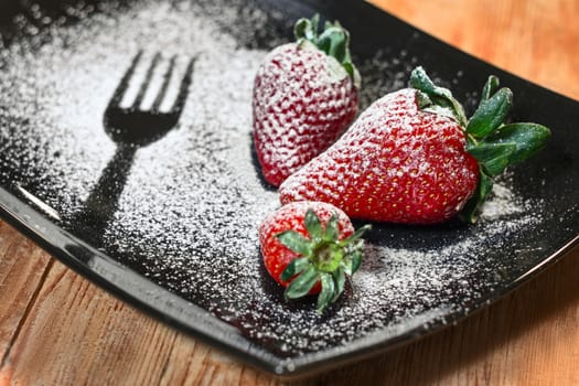 three strawberries sprinkled with sugar on a black plate and wooden base