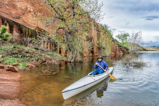 a senior paddler in an decked expedition canoe approaching rocky sandstone shore - Horsetooth Reservoir near Fort Collins, Colorado