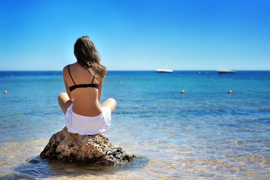 Young woman sitting on sand and looking to a sea.