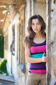 beautiful brunette young woman standing near old stone wall.