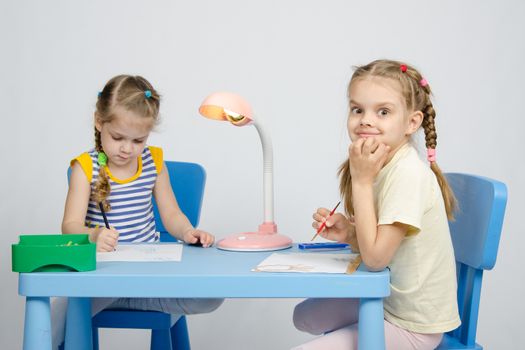 Two girls of four and six years of sitting at the table and draws and paints and pencils