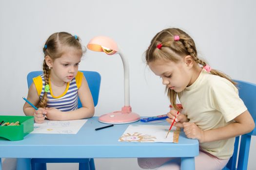 Two girls of four and six years of sitting at the table and draws and paints and pencils