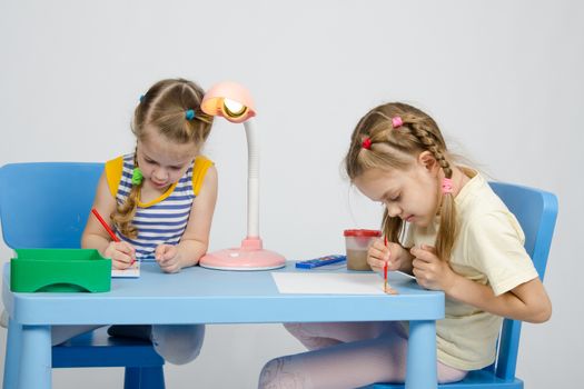 Two girls of four and six years of sitting at the table and draws and paints and pencils