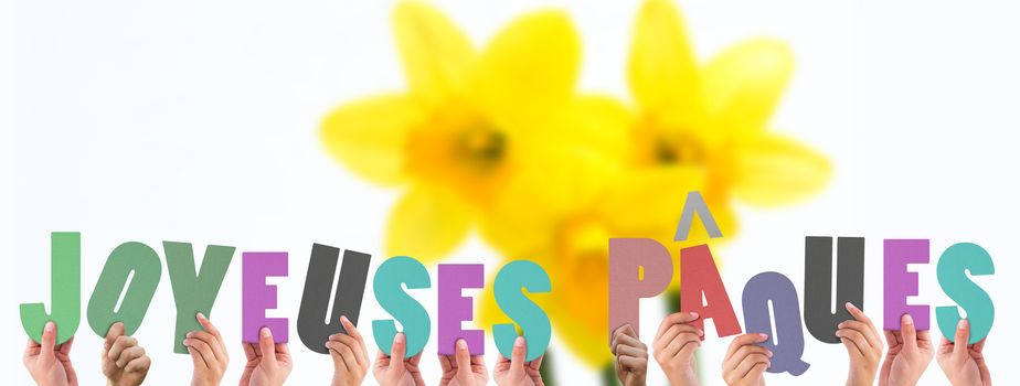 Hands holding up joyeuses pasques against pretty yellow daffodils with copy space